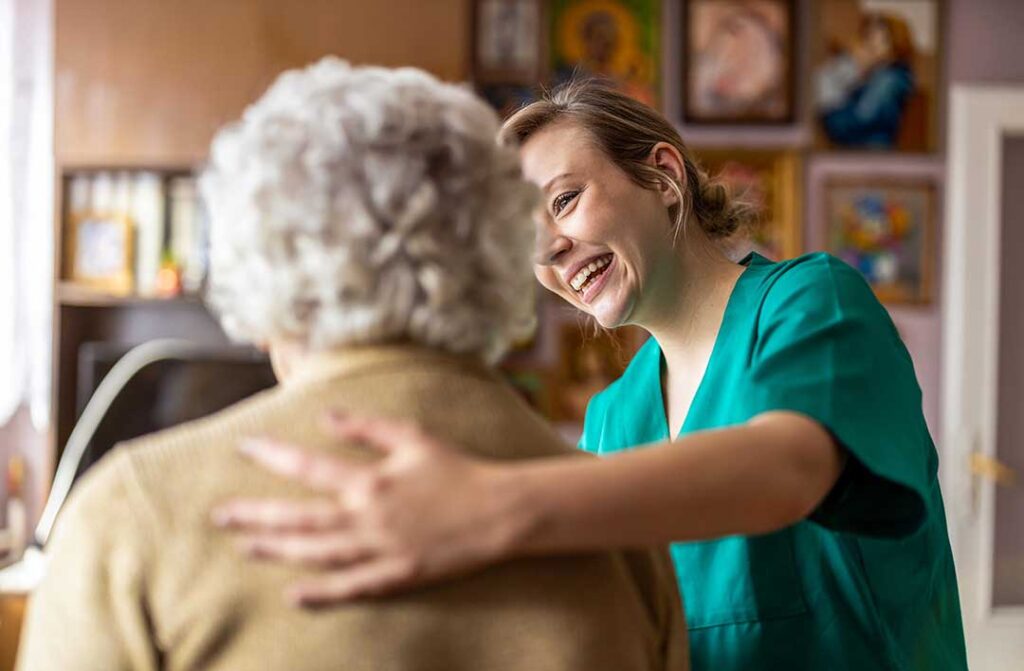 Three older adults and a young volunteer smiling together at a craft table in a comfortable community room.