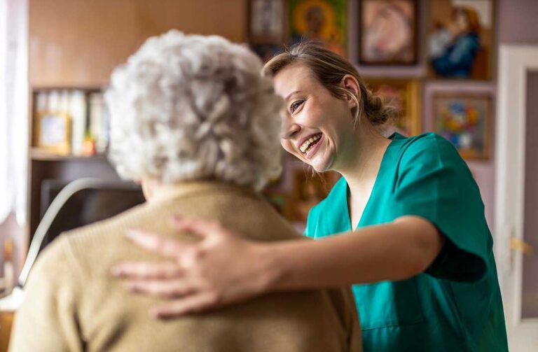 Three older adults and a young volunteer smiling together at a craft table in a comfortable community room.